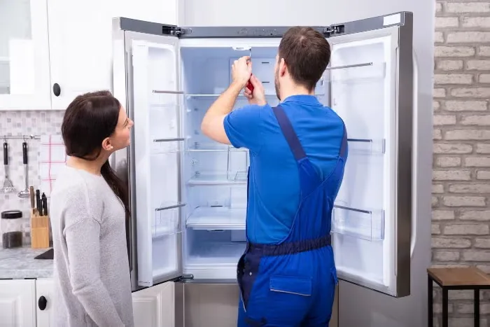 NK Fridge Repair technician inspecting refrigerator coils
